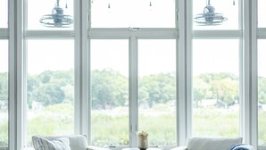 Ein modernes Wohnzimmer mit Deckenventilator, großen Fenstern, zwei weißen Sofas und einem blauen Teppich.
