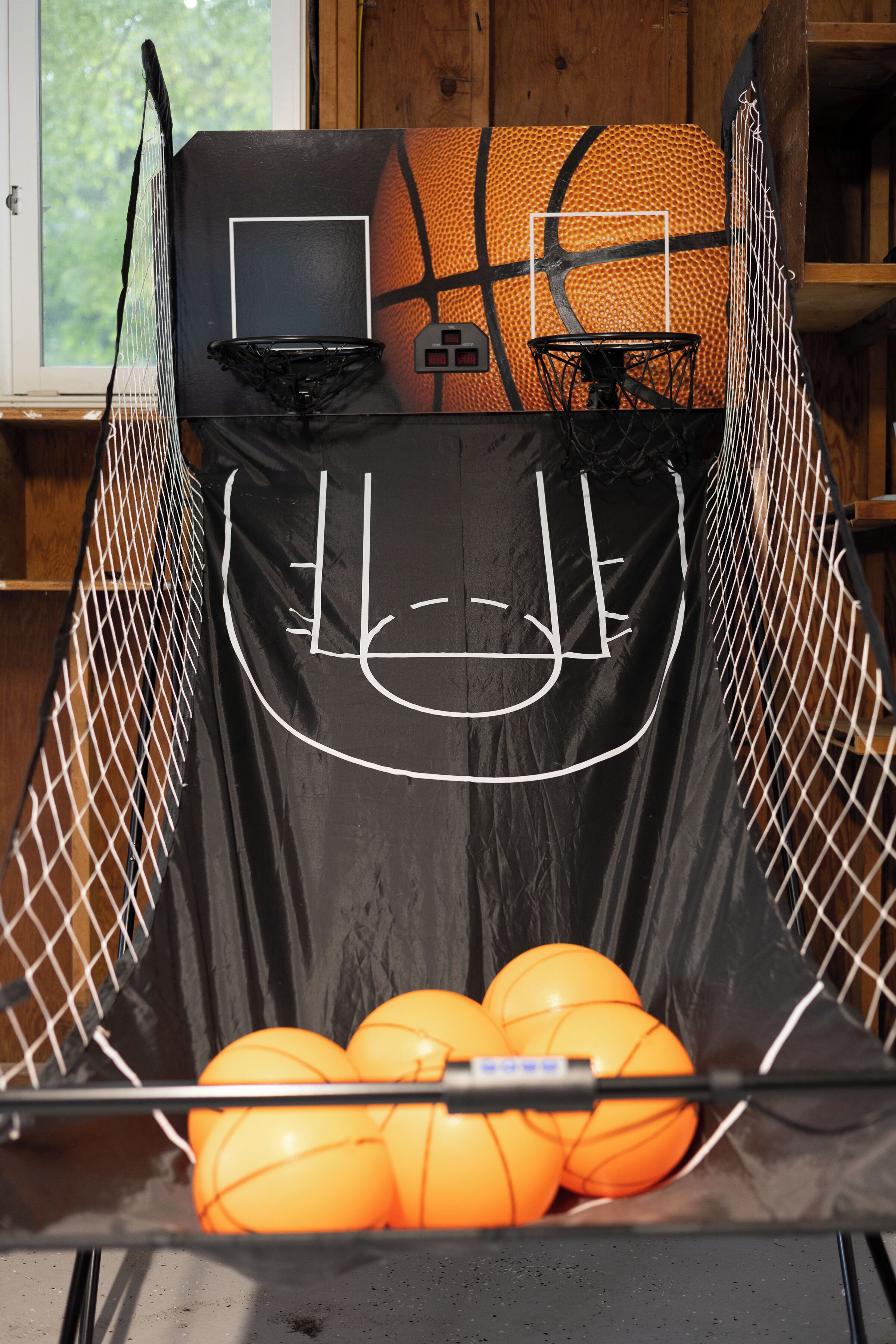 Un panier de basket avec un filet, un ballon de basket et un tapis noir avec des lignes blanches.
