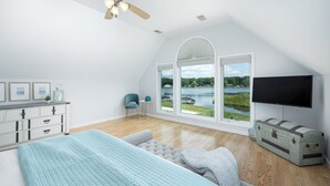 Ein Schlafzimmer mit einem Bett, einer Kommode, einem Sessel, einem Fernseher und einem großen Fenster mit Seeblick.