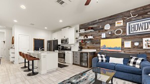Une cuisine moderne avec des meubles blancs, un îlot central doté de tabourets, un canapé bleu et un mur rustique agrémenté de diverses décorations.