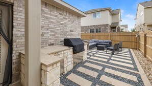 Une terrasse extérieure dotée d’une cheminée en pierre, d’un barbecue et d’un espace salon avec un canapé et des fauteuils.