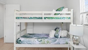 A bunk bed with a tropical leaf-patterned bedspread, a white door, and a bedside lamp on a small table. - The Beach Bungalow by Book That Condo (Panama City Beach)