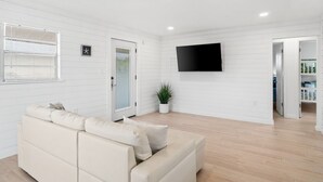 A modern living room with a beige sofa, a flat-screen TV mounted on the wall, and a potted plant. - The Beach Bungalow by Book That Condo (Panama City Beach)