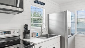 A kitchen with stainless steel appliances, a window with blinds, and a sign that reads "BEACH VIBES". - The Beach Bungalow by Book That Condo (Panama City Beach)