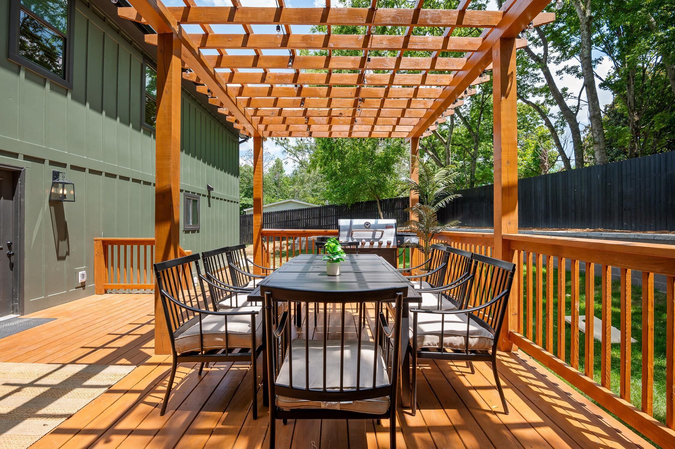Un patio exterior con piso de madera, una mesa con sillas y una estructura de pérgola.