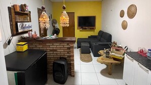 A compact living space with a kitchen area, a black sofa, a small coffee table, and a TV mounted on the wall. - Cozy house in Tutoia-Ma, close to everything, beaches, kite surfing, dunes. (Tutóia)