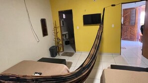A room with a hammock bed, a television mounted on the wall, and a door leading to another room. - Cozy house in Tutoia-Ma, close to everything, beaches, kite surfing, dunes. (Tutóia)
