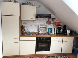 A compact kitchen with white cabinets, a built-in oven, a coffee maker, and a kettle on the countertop.