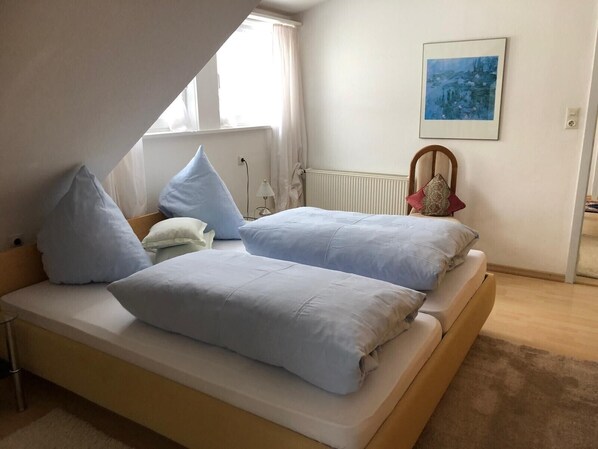 A bedroom with two beds, a radiator, a window, and a painting on the wall.