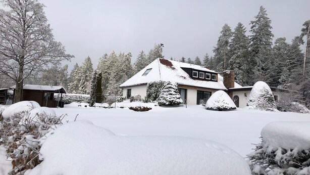 Une maison recouverte de neige, avec un toit en pente, un petit porche et une cheminée.