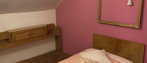 A bedroom with a sloped ceiling, a wooden bed frame, a pink wall, and a chandelier.