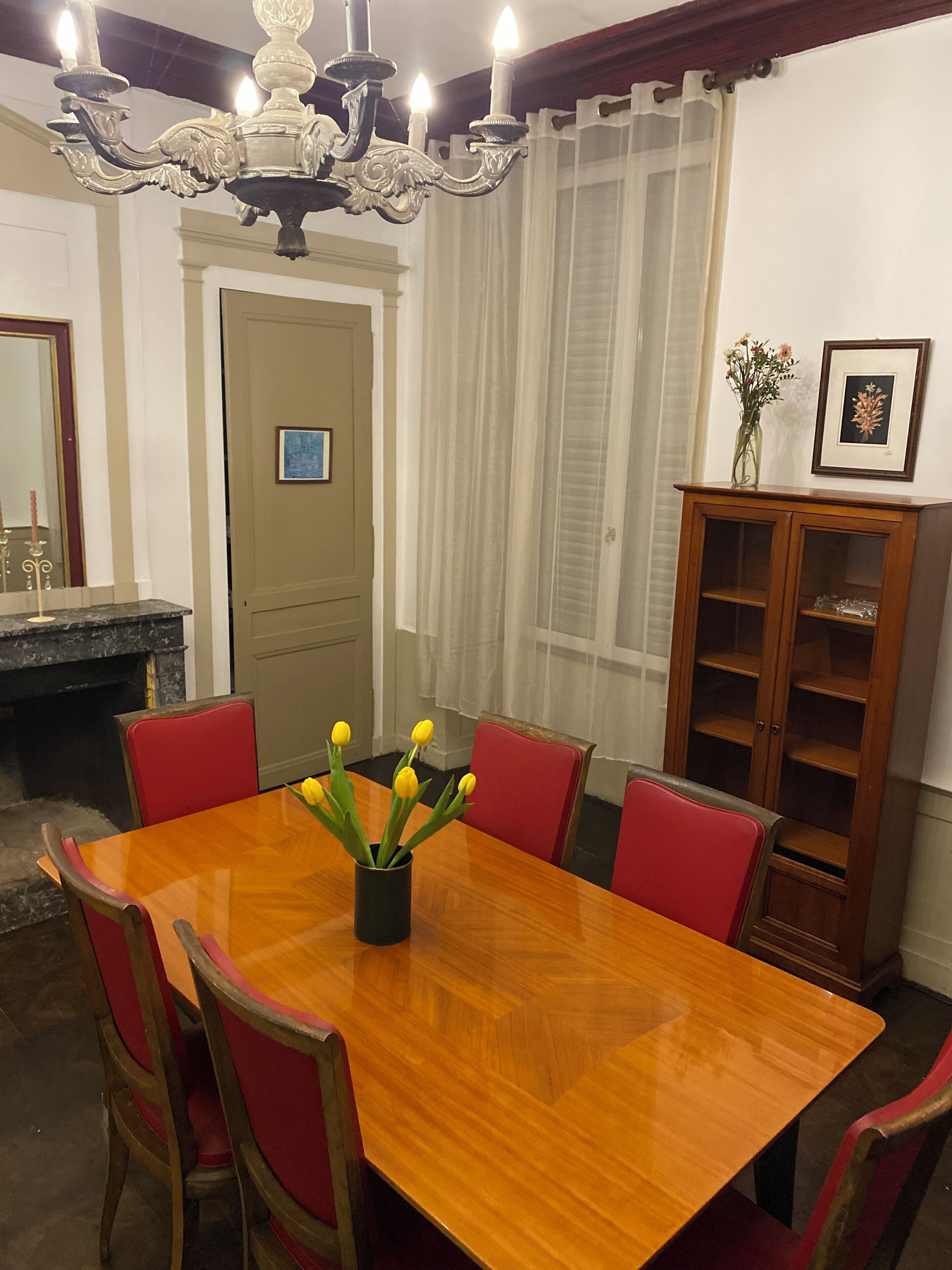 A dining room with a wooden table, red chairs, a chandelier, a cabinet, and a door with a picture on it.