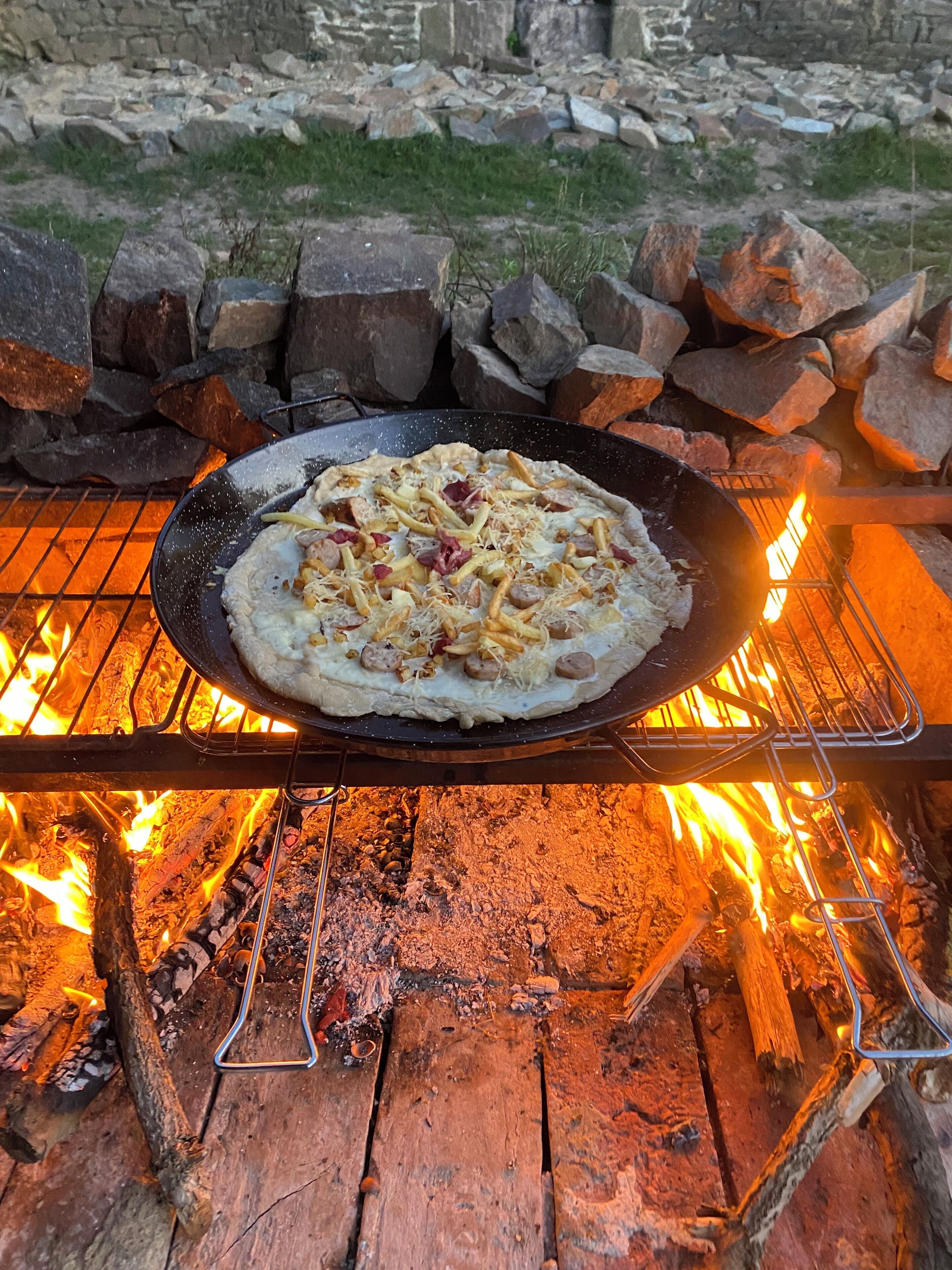 Une pizza cuite sur un gril au-dessus d’un feu de bois.