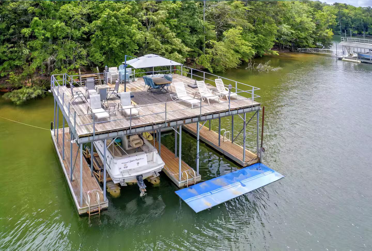 Una terraza flotante con asientos y zona cubierta, rodeada de agua y vegetación.