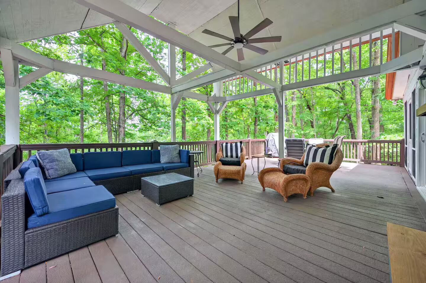 A covered outdoor seating area with a sofa, chairs, and a table, surrounded by trees.