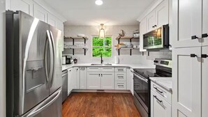 A modern kitchen with white cabinetry, stainless steel appliances, and a wooden floor.