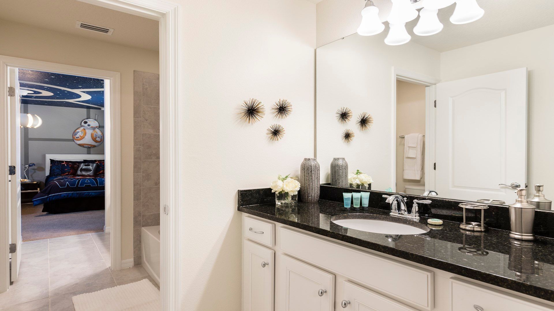 A modern bathroom with a large mirror, black countertop, and decorative wall sconces.