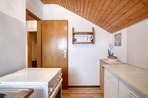 Een compacte keuken met een houten plafond, een witte koelkast, een houten kast en een klein plankje met een koffiezetapparaat.