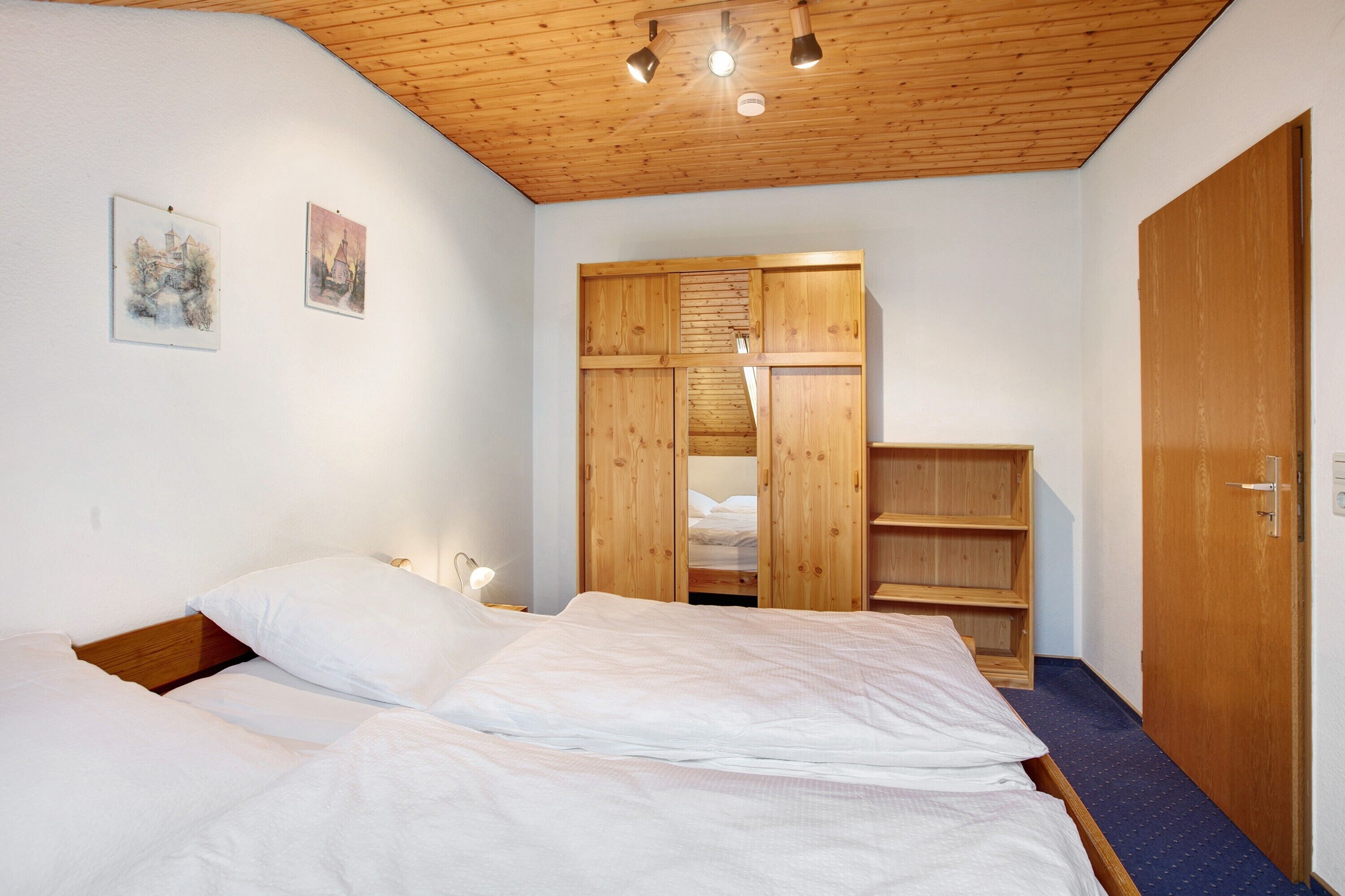 Una camera da letto con soffitto in legno, un letto con biancheria bianca, un armadio in legno e una porta.