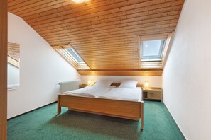 A bedroom with a wooden ceiling, skylights, a bed, bedside tables, and a radiator.