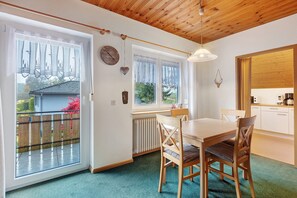 A dining area with a wooden table and chairs, a window with curtains, a clock, and a radiator.