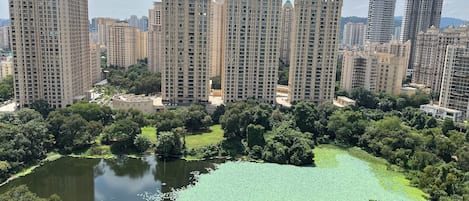 A high-rise residential building complex with multiple apartment buildings, surrounded by lush greenery and a small pond.