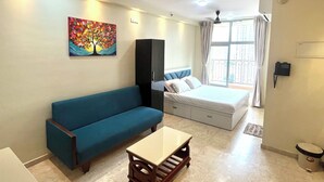 A hotel room with a bed, a blue sofa, a small table, a cabinet, a ceiling fan, and a window with curtains.