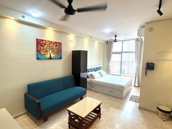 A hotel room with a bed, a blue sofa, a small table, a cabinet, a ceiling fan, and a window with curtains.