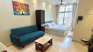 A modern room with a blue sofa, a bed with a headboard, a small table, and a painting on the wall.