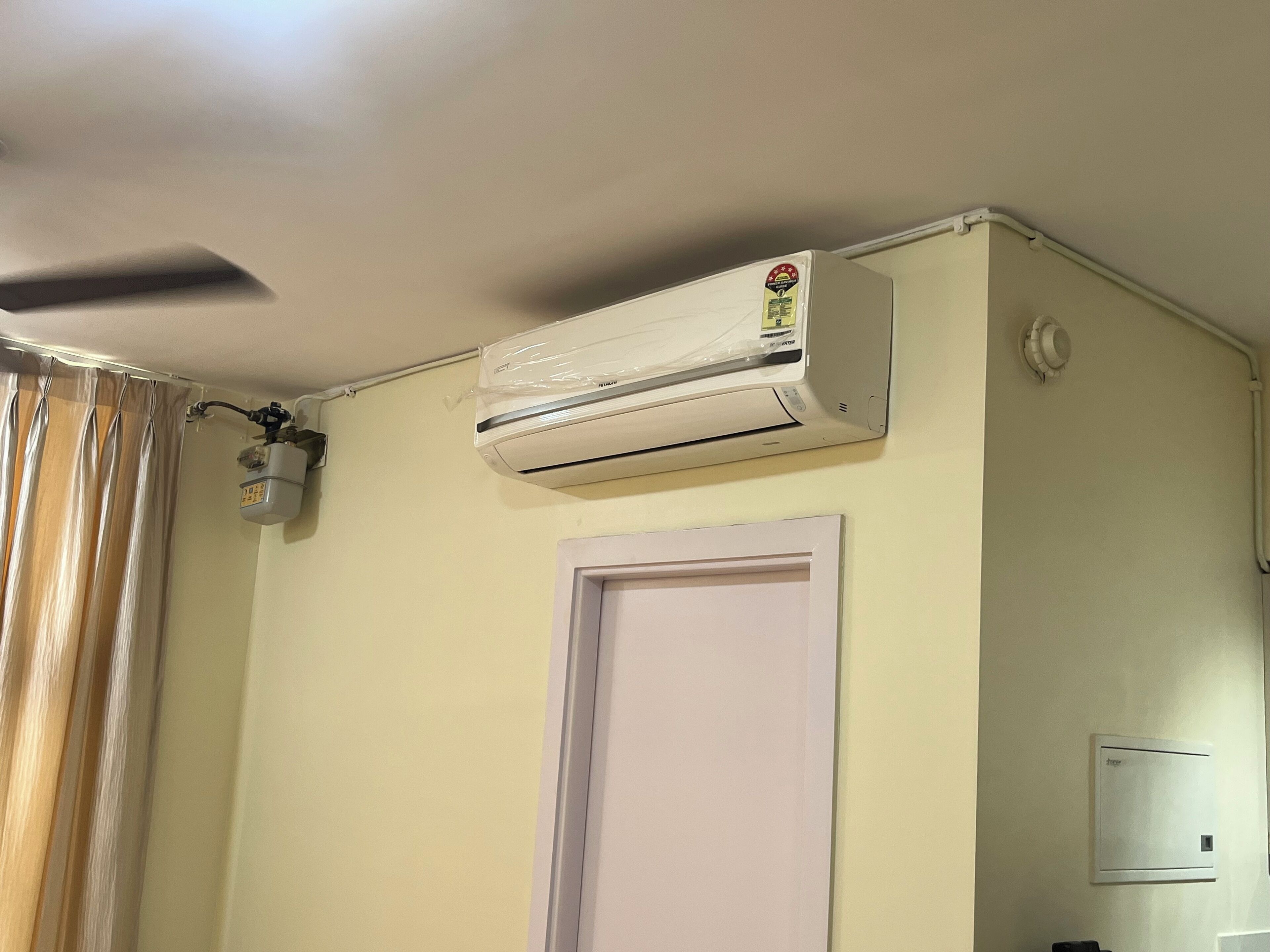 Ein Zimmer mit Deckenventilator, Klimaanlage, einer Lampe und einer Tür.