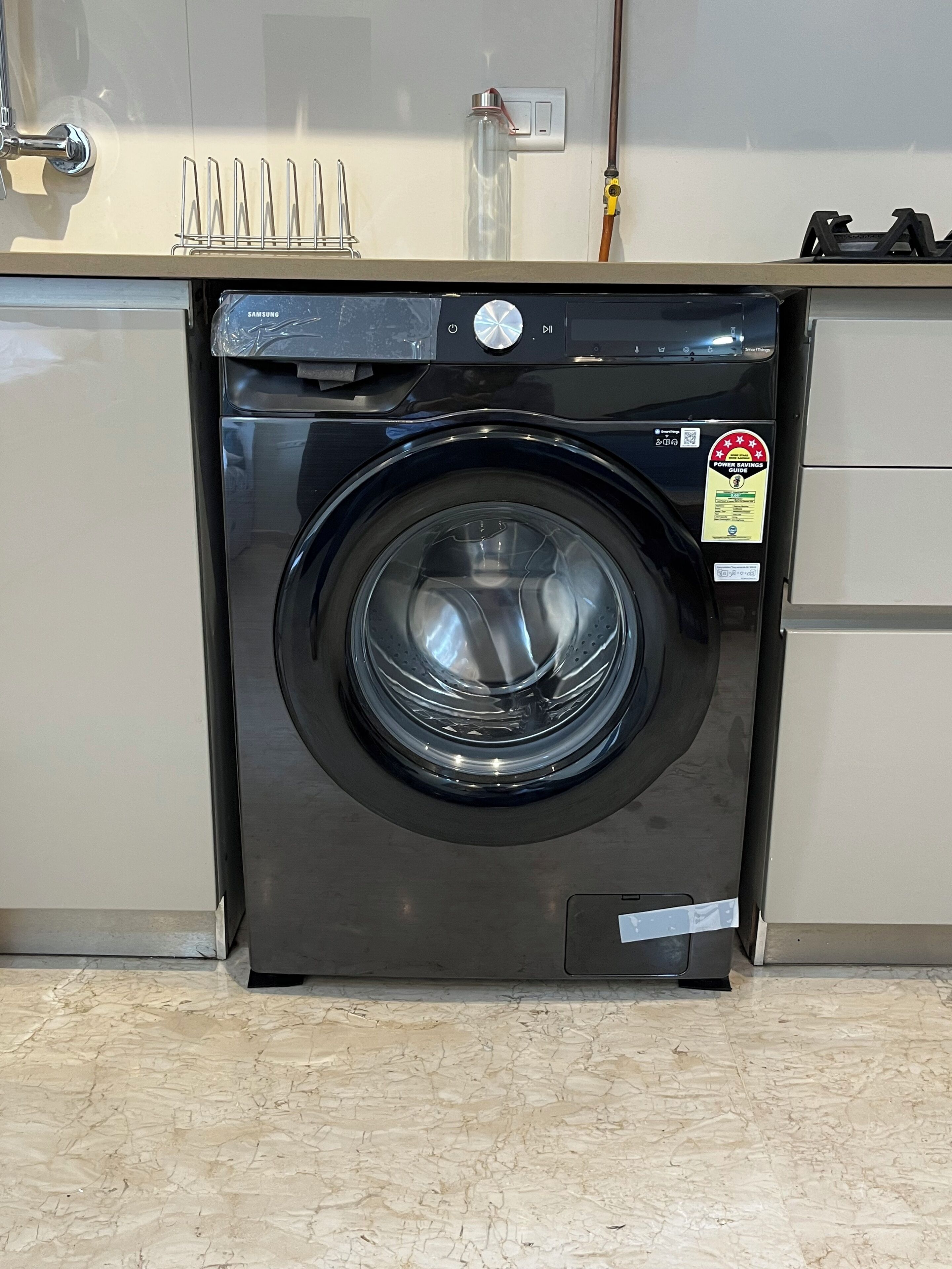A black front-loading washing machine with a power savings sticker, a stainless steel door, and a control panel with a power button and a dial.