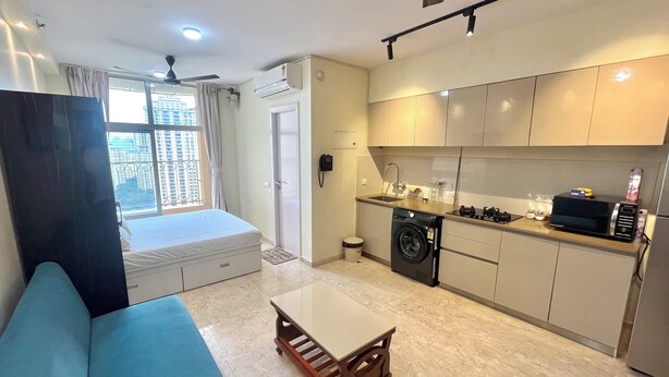 A compact living space with a sofa, a small table, a washing machine, and a kitchenette.