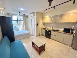 A compact living space with a sofa, a small table, a washing machine, and a kitchenette.