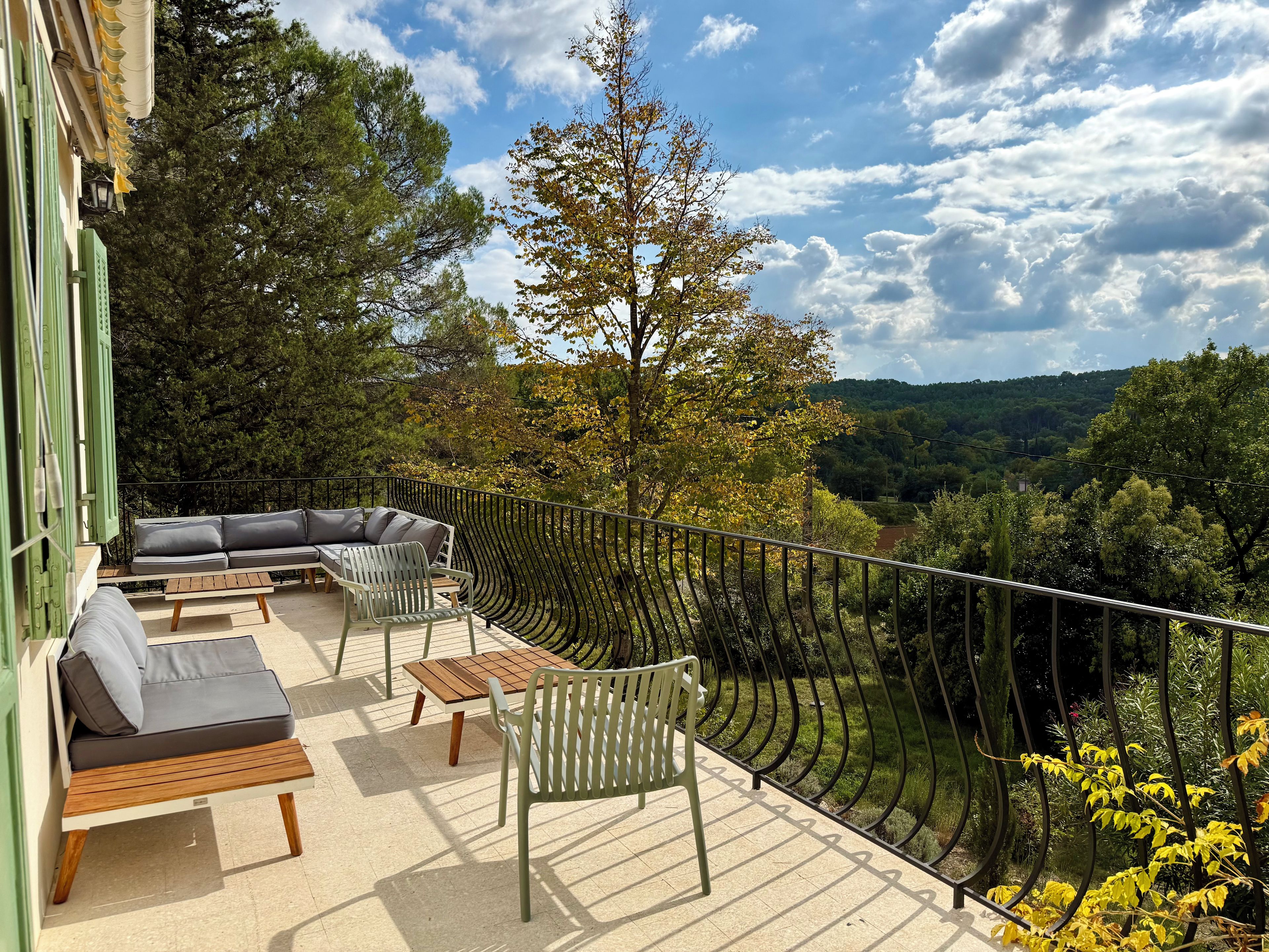 Een balkon met een bank, stoelen en een tafel, met uitzicht op een bebost landschap.
