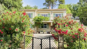 A two-story house with a balcony, surrounded by lush greenery and flowering plants. - Family villa - Breathtaking view of the vineyards - private, fenced pool. (Entrecasteaux)