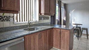 Una cocina con encimeras de granito, armarios de madera, lavavajillas y una ventana con persianas.