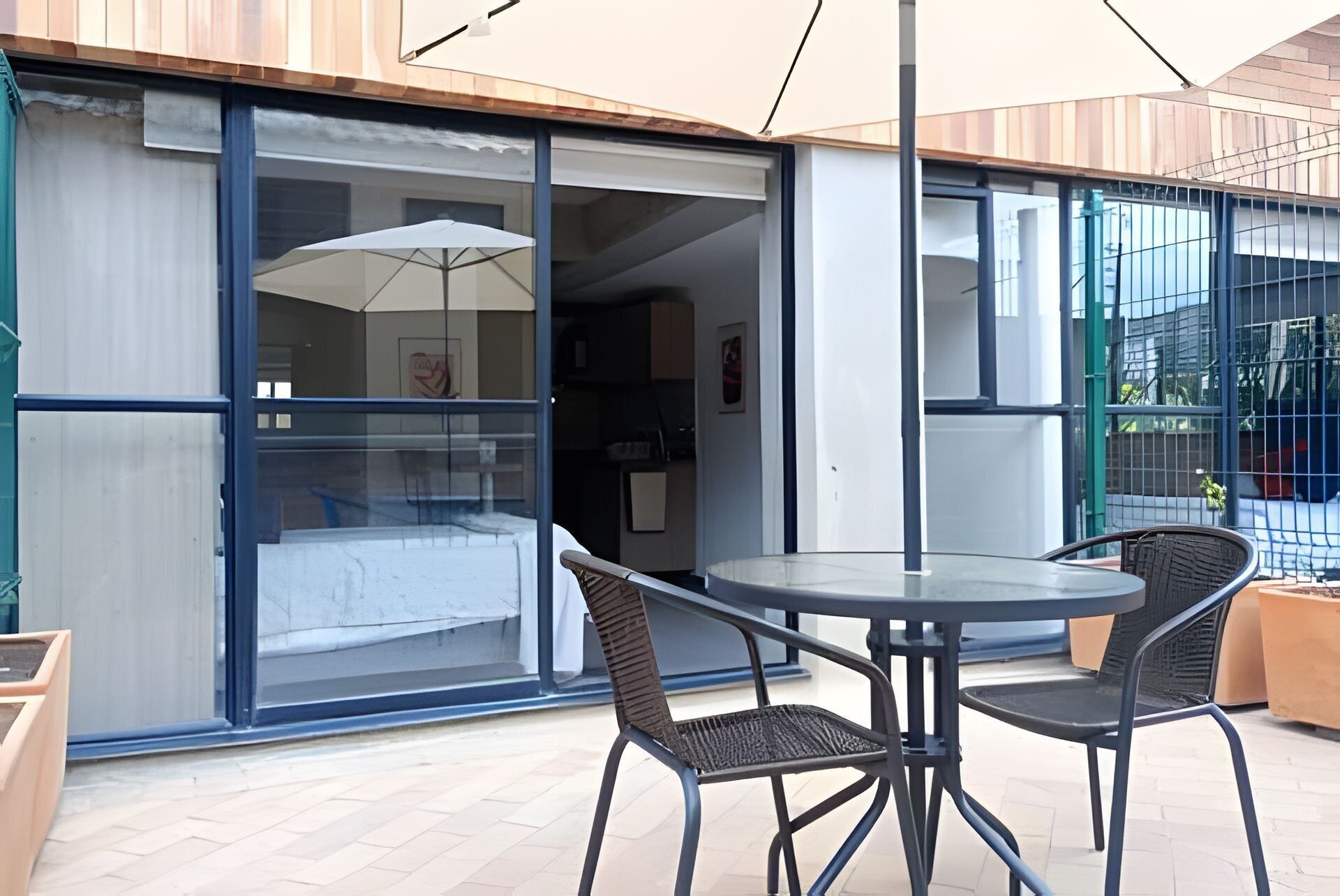 A modern outdoor seating area with a table and chairs, a glass door entrance, and a view of the interior.
