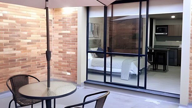A balcony with a table and chairs, a sliding glass door leading to a bedroom with a bed and a kitchen area visible. - Spatium 134 (Bogotá)