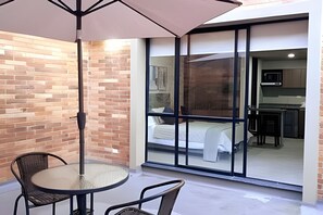 A balcony with a table and chairs, a sliding glass door leading to a bedroom with a bed and a kitchen area visible. - Spatium 134 (Bogotá)