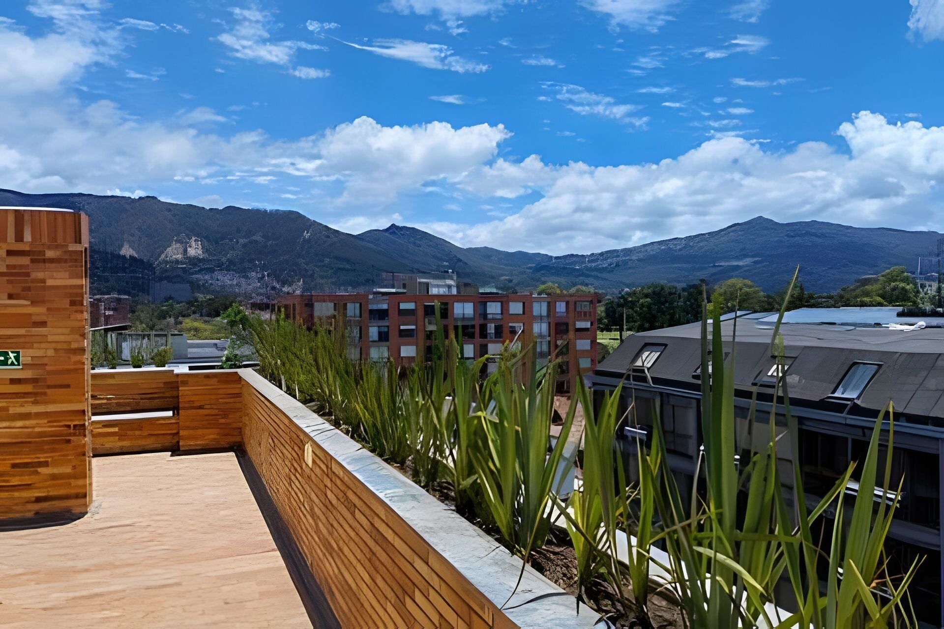 Eine Dachterrasse mit Holzboden, Blick auf Berge und ein modernes Gebäude mit vielen Fenstern.