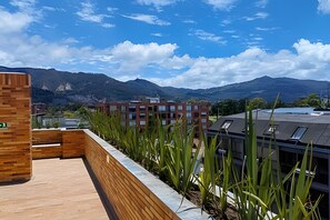 En takterrass med trägolv, utsikt över bergen och en modern byggnad med många fönster.