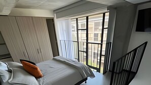 A modern bedroom with a bed, a small table, a chair, a balcony with a railing, and a staircase. - Spatium 134 (Bogotá)
