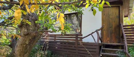 A rustic wooden structure with a wooden door and steps leading up to it, surrounded by trees with yellow leaves.
