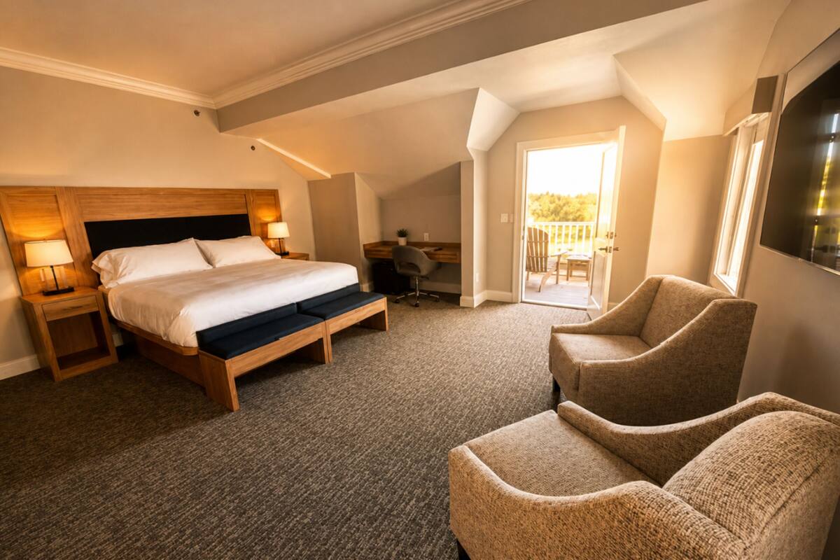 Habitación de hotel con una cama grande, lámparas de noche, un escritorio, dos sillones y un balcón.