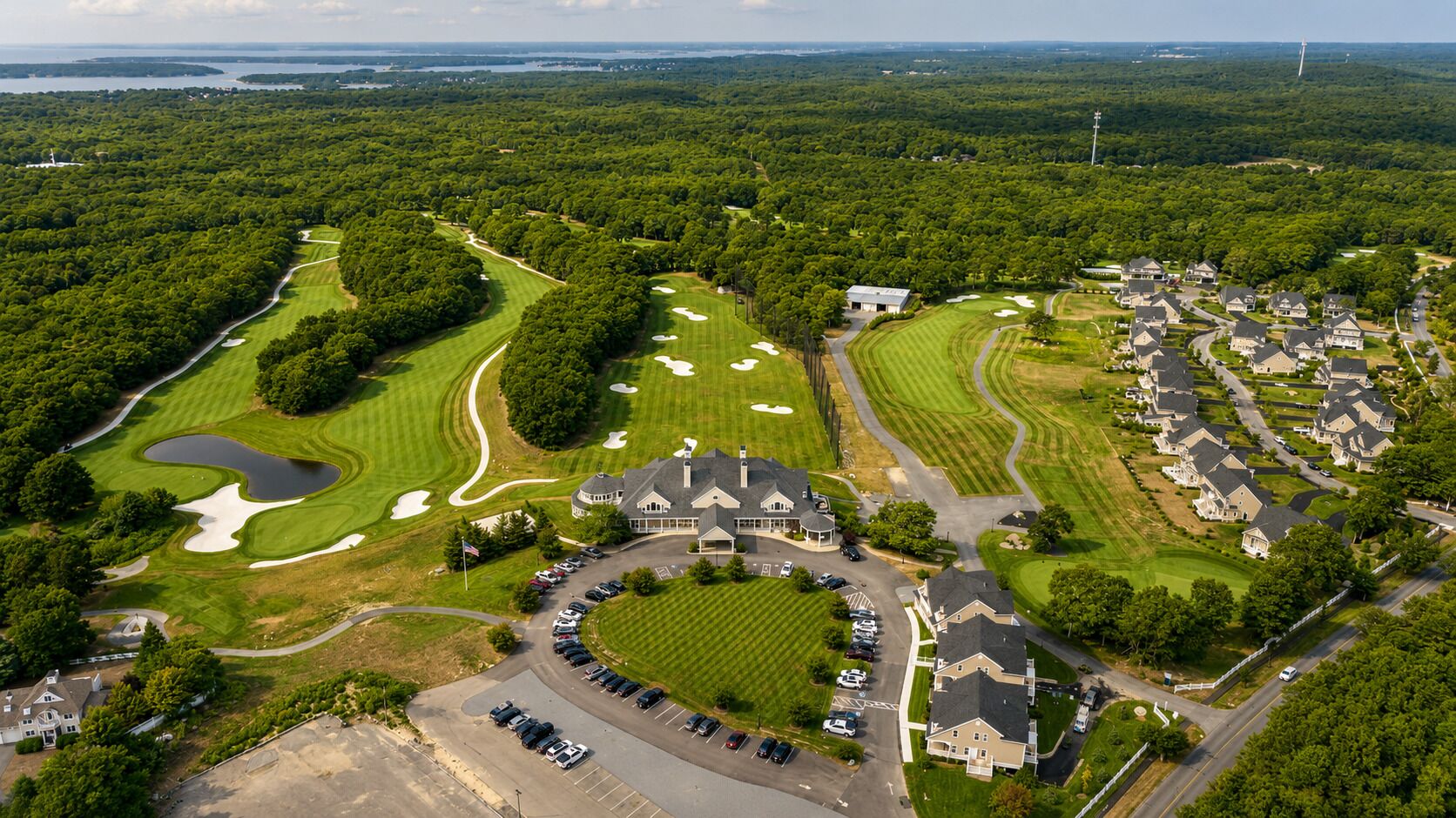 An aerial view of a golf course with a clubhouse, residential area, and parking lot.