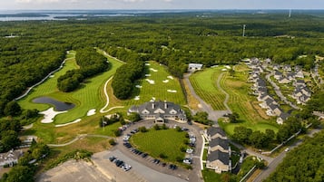 Vue aérienne d’un terrain de golf avec un club-house, une zone résidentielle et un parking.