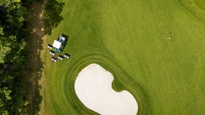 Vista aérea de un campo de golf con un búnker de arena y un carrito de golf.