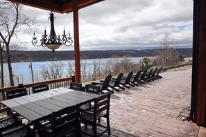 An outdoor patio with tables and chairs, a hanging chandelier, and a view of a lake and hills.