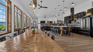 Une cuisine spacieuse avec une longue table en bois, des meubles noirs et des luminaires suspendus.