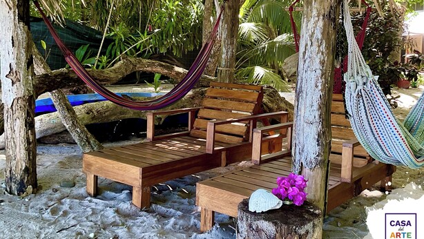 A wooden bench and hammock under a thatched roof, surrounded by tropical plants. - Oceanfront Artistic Escape in Cabuya (Cabuya)